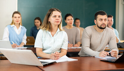 Group of adult students sitting at tables in classroom and studying.