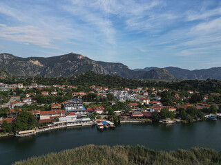 Fototapeta premium Dalyan waterfront in Aegean Mugla province Lined with cafes boats and houses River flows calmly with green hills and mountains surrounding town