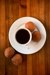 Top view of a cup of black coffee with homemade donuts on a white plate and wooden table. Warm, cozy breakfast or coffee break scene with rustic vibes.