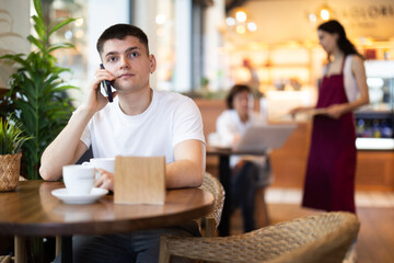 Young man talking on mobile phone and drinking coffee in cafe