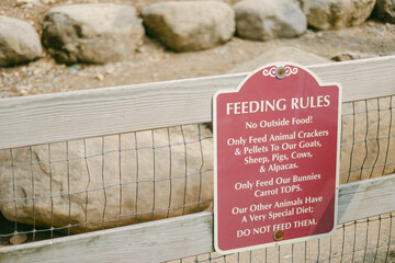 Feeding rules sign at a petting zoo outlining animal dietary restrictions near a rock formation