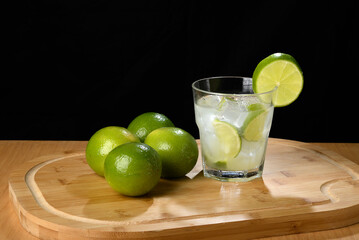 Refreshing caipirinha with lime and ice on a wooden board