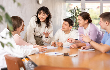 Group of girls and boys studying in school, sitting around desks and attending teacher lecture