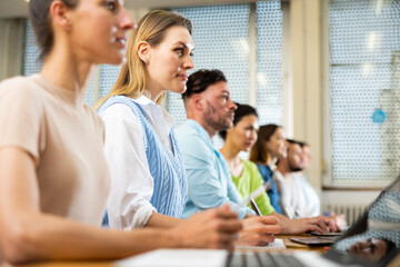 Portrait of a young girl student studying with fellow students in a university auditorium during classes on a laptop and ..writing a synopsis in a copybook