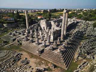 Grand podium of the temple of apollo shows deep steps and column drums, pillars cast long shadows across the stylobate, the town of didim frames the ruins, enduring archaeology of Turkey inspires