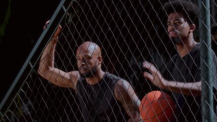 Men playing basketball on outdoor court behind fence - Powered by Adobe