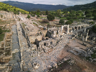 Aerial view along Curetes Street shows marble paving, arches and storefronts, visitors walk the ancient route in Ephesus, hills frame the city, heritage of Turkey preserved among stones
