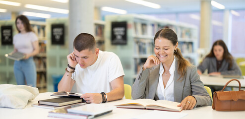 Young guy and young woman students reading book sitting at table in library