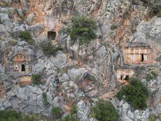 Close cluster of Lycian cliff tombs above a wooded gorge near Dalyan in Mugla Turkey geometric facades show ancient craftsmanship amid shrubs and limestone crags Mediterranean archaeology scenery