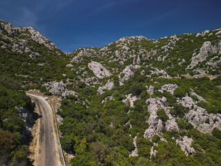 Mountain pass through maquis and limestone in Aegean region Mugla Province Bozburun Peninsula Turkey Curving asphalt road hugs rocky slopes Bright noon light Clear summer weather Remote landscape