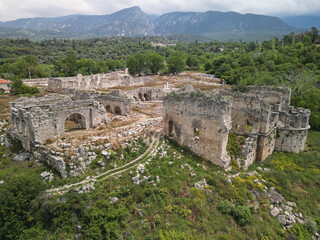 Tlos ruins spread across a hillside in Fethiye, Mugla Province, Turkey under midday light with mountains beyond Stone arches and basilica walls trace Roman and Byzantine layers in a rural valley