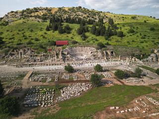 Ancient odeon of Ephesus stands beside a paved colonnade, visitors explore the marble street, green hillside frames the site, heritage of western Turkey, ideal for history and travel imagery