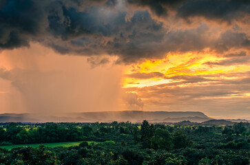 Beautiful scenery of the rainy season, evening light shining through rain clouds, rain, mountains, green rice fields and trees in the countryside of Chiang Rai Province, Thailand.
