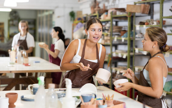 Positive young girls in apron processing clay bowls in carpenter's workshop