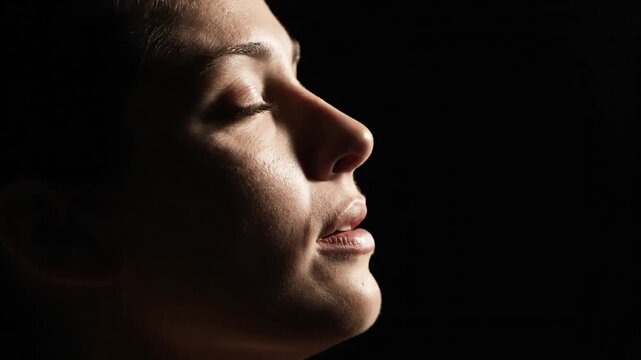Profile of a persons face with closed eyes and slightly open mouth dramatically lit against a dark background