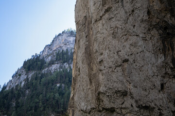 vertical shot capturing the towering rock faces of Romania's Bicaz Canyon (Cheile Bicazului), with a closer cliff in the foreground and a distant, forest-covered mountain