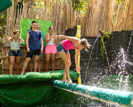 Caucasian woman walking over water pool on crossbar to pass obstacle course in adventure park. - Powered by Adobe