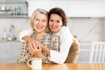 Friendly middle-aged woman asking for forgiveness to offended mature woman sitting in the kitchen