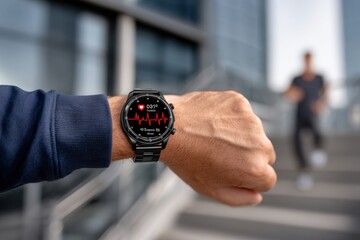 Close up of a man's wrist with a modern smartwatch displaying health metrics, fitness data, with a jogger in the background during an outdoor workout.