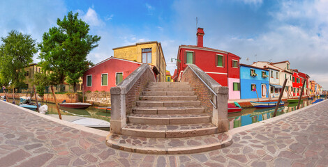 Colorful houses along a canal on Burano Island in Venice Italy with boats moored on both sides.