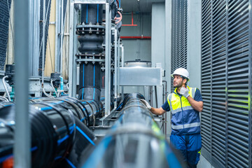 Industrial engineering technician worker working maintenance building exterior plumbing systems. Male engineer in safety uniform speaking on radio and checking pipeline valves at construction site.