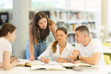 Group of student sits at table in library and studies, reads books and takes notes, makes summary, deliberative meeting, collective work. Preparation for exams, educational process, additional classes