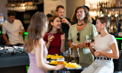 Happy mens and womens drinking beer and eating crisps, laughing and spending time together in a bar