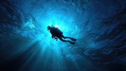 Silhouetted scuba diver ascends, backlit by sunbeams penetrating deep, blue ocean water, creating a dramatic underwater scene