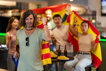 Group of friends fans watching match cheering with flags of Catalonia and Spain in bar