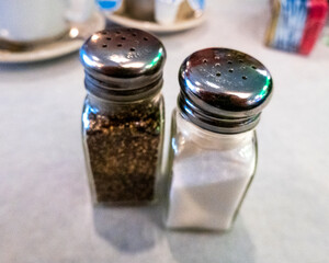 Close-up of glass salt and pepper shakers resting on a diner’s table, set atop a crisp white paper placemat, capturing a classic, timeless touch of casual dining..