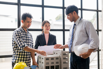 Architects and construction engineer discussing building project using scale model and blueprints
