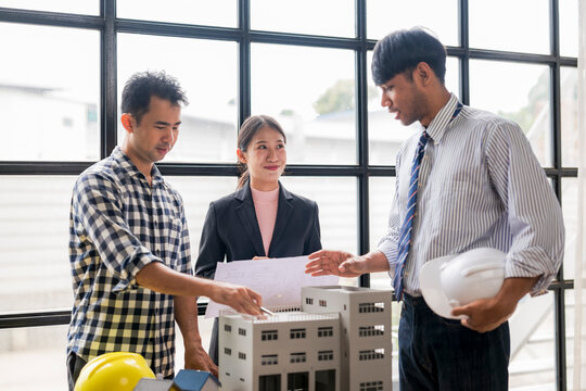 Architects and construction engineer discussing building project using scale model and blueprints