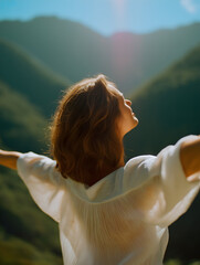 A woman stands with outstretched arms, basking in the sunlight amidst mountains, embodying a sense of freedom and connection with nature.