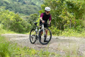 Fototapeta premium Latino man in his 30s walking with road bike on gravel path