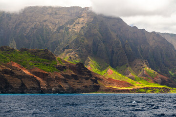 Towering cliffs of the Na Pali Coast on Kauai, Hawaii, rise dramatically from the shoreline, viewed from the waters of the Pacific Ocean.