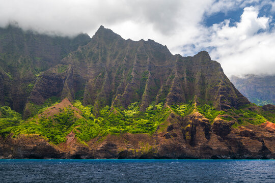 Towering cliffs of the Na Pali Coast on Kauai, Hawaii, rise dramatically from the shoreline, viewed from the waters of the Pacific Ocean.