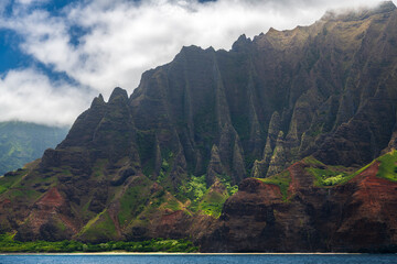 Towering cliffs of the Na Pali Coast on Kauai, Hawaii, rise dramatically from the shoreline, viewed from the waters of the Pacific Ocean.