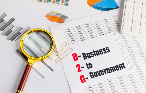 Paper with b2g business to government text on desk with magnifying glass, charts, tables and calculator