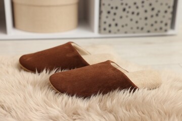 Stylish brown slippers on fluffy carpet indoors, closeup