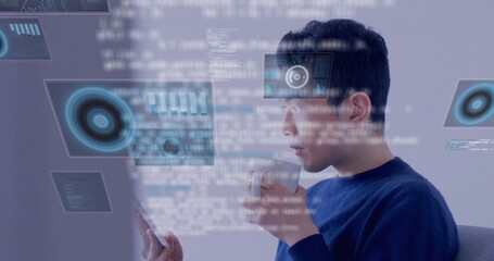 Asian man in blue sweater analyzing holographic code charts in office, with white mug and tablet