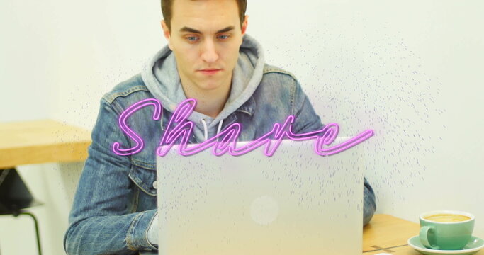 Typing man wearing denim jacket at cafe, with laptop showing neon-pink Share text and green mug