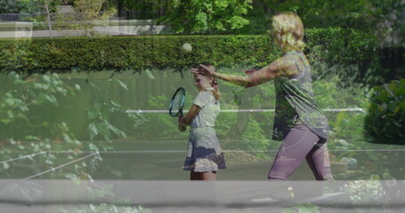 Tossing tennis ball mother in sportswear coaching daughter on home court with racket net plants