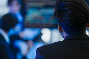 From behind, a manager or director watches a virtual team meeting on a large screen. A concept for modern leadership, global business strategy, data analysis, and remote collaboration.