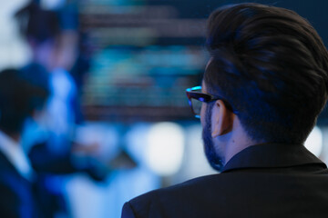 From behind, a manager or director watches a virtual team meeting on a large screen. A concept for modern leadership, global business strategy, data analysis, and remote collaboration.