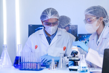 A team of diverse scientists discusses experimental results in a high-tech lab. A male researcher presents a sample in a test tube while colleagues analyze data for a new discovery.