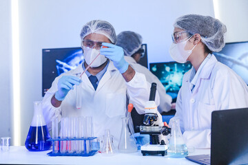 A team of diverse scientists discusses experimental results in a high-tech lab. A male researcher presents a sample in a test tube while colleagues analyze data for a new discovery.
