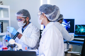 A team of diverse scientists discusses experimental results in a high-tech lab. A male researcher presents a sample in a test tube while colleagues analyze data for a new discovery.