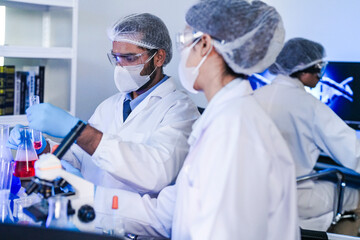 A team of diverse scientists discusses experimental results in a high-tech lab. A male researcher presents a sample in a test tube while colleagues analyze data for a new discovery.