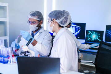 A team of diverse scientists discusses experimental results in a high-tech lab. A male researcher presents a sample in a test tube while colleagues analyze data for a new discovery.