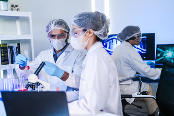A team of diverse scientists discusses experimental results in a high-tech lab. A male researcher presents a sample in a test tube while colleagues analyze data for a new discovery.